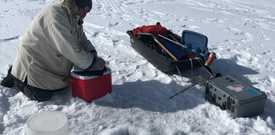 Bénévole LakeKeepers à genoux sur le lac Chestermere gelé avec équipement de surveillance de l'eau en hiver